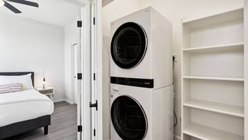A bedroom with a bed, a wall-mounted washer and dryer, and a white shelving unit.