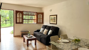 A living room with a sofa, a glass coffee table, a dining table set with plates and glasses, and a window with a view of greenery. - El Pinar House: Tranquility, Family, and Nature (Jardín)