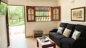 A living room with a black sofa, a wooden coffee table, a potted plant, and a window with wooden shutters. - El Pinar House: Tranquility, Family, and Nature (Jardín)