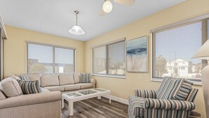 A living room with a beige sofa, a striped armchair, a glass coffee table, and large windows offering views of the outside.