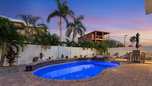 A swimming pool with a tiled deck, surrounded by palm trees and a white fence.