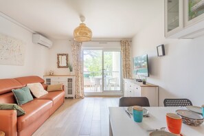 A modern living room with a sofa, a dining table with cups and plates, a TV, and a balcony with a view.