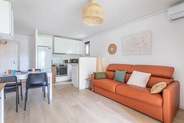 A modern kitchen with white cabinets, a dining area with a table and chairs, and a living area with a sofa and a decorative wall piece.
