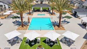 Un espace piscine agrémenté de chaises longues et de parasols, entouré de palmiers et de maisons modernes.