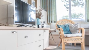 A modern room with a TV, a wicker chair, a white dresser, and a window with curtains.