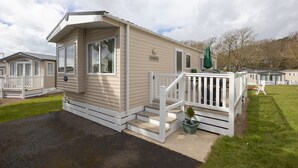 A mobile home with a front porch and a small deck, surrounded by other similar homes.