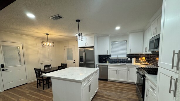 A modern kitchen with white cabinetry, a central island, a stainless steel refrigerator, and a built-in oven. - A Home Away From Home - Rest, Relax, & Enjoy (Alexandria)