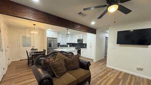 A modern living room with a dark leather sofa, a dining area, and a kitchen with white cabinets and a black backsplash. - A Home Away From Home - Rest, Relax, & Enjoy (Alexandria)