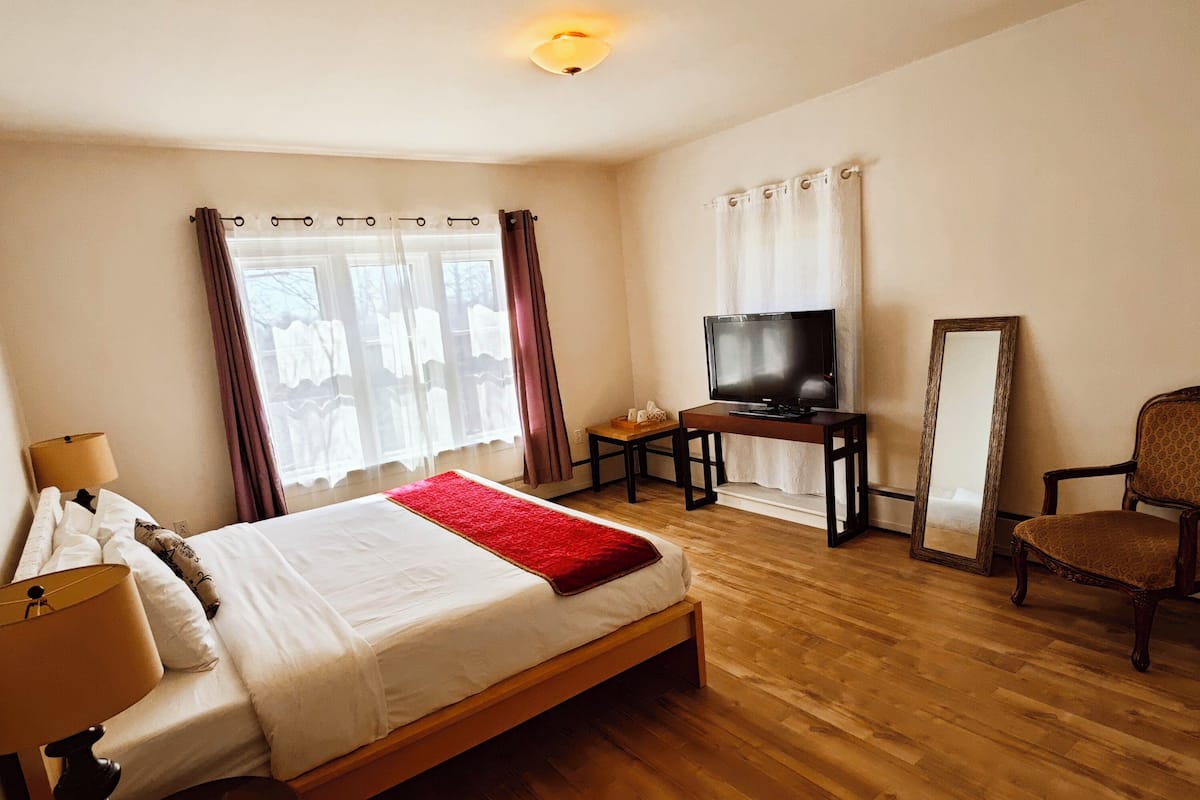 A hotel room with a large bed, a TV, a chair, and a mirror.