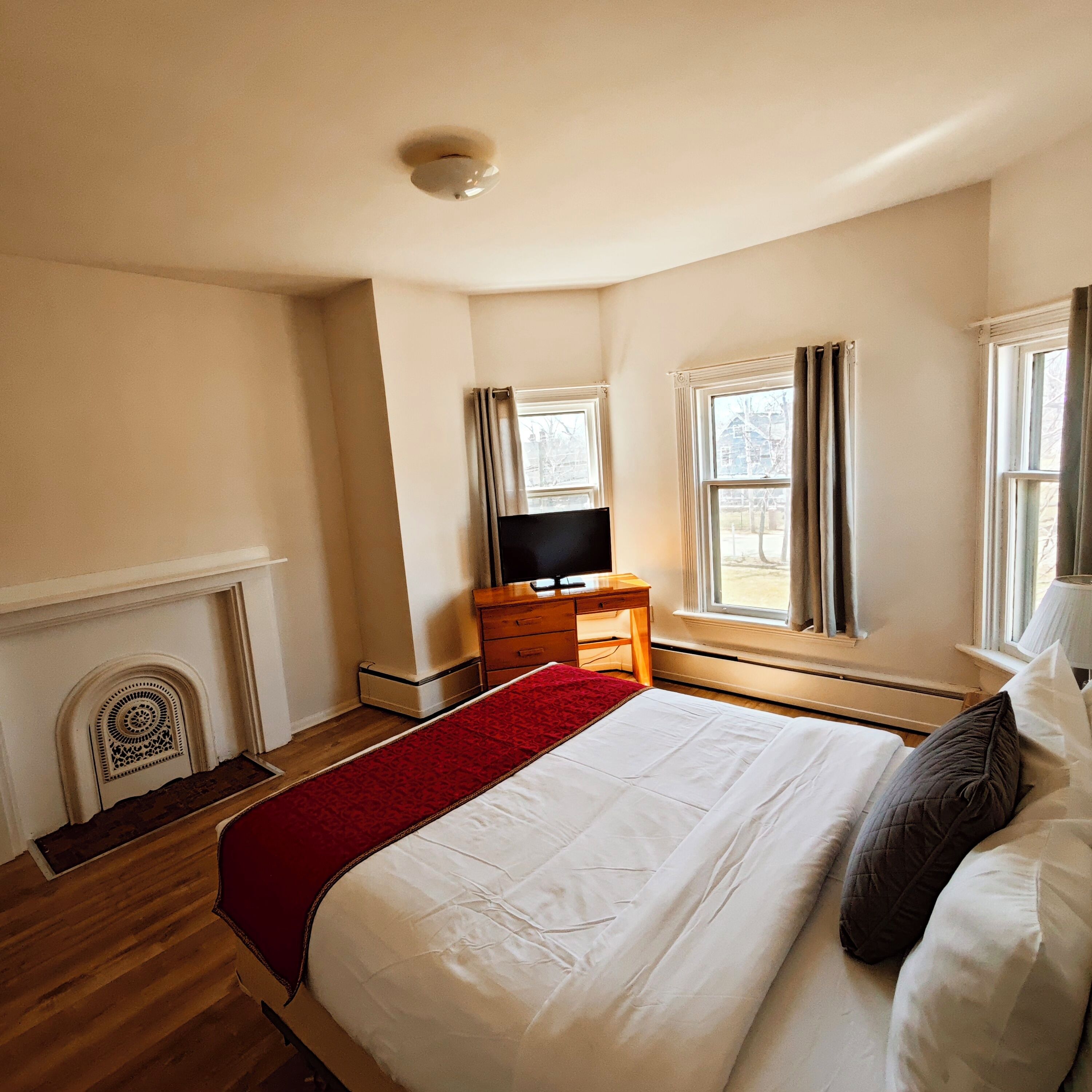 Un dormitorio con cama, televisión, chimenea y ventanas con cortinas.