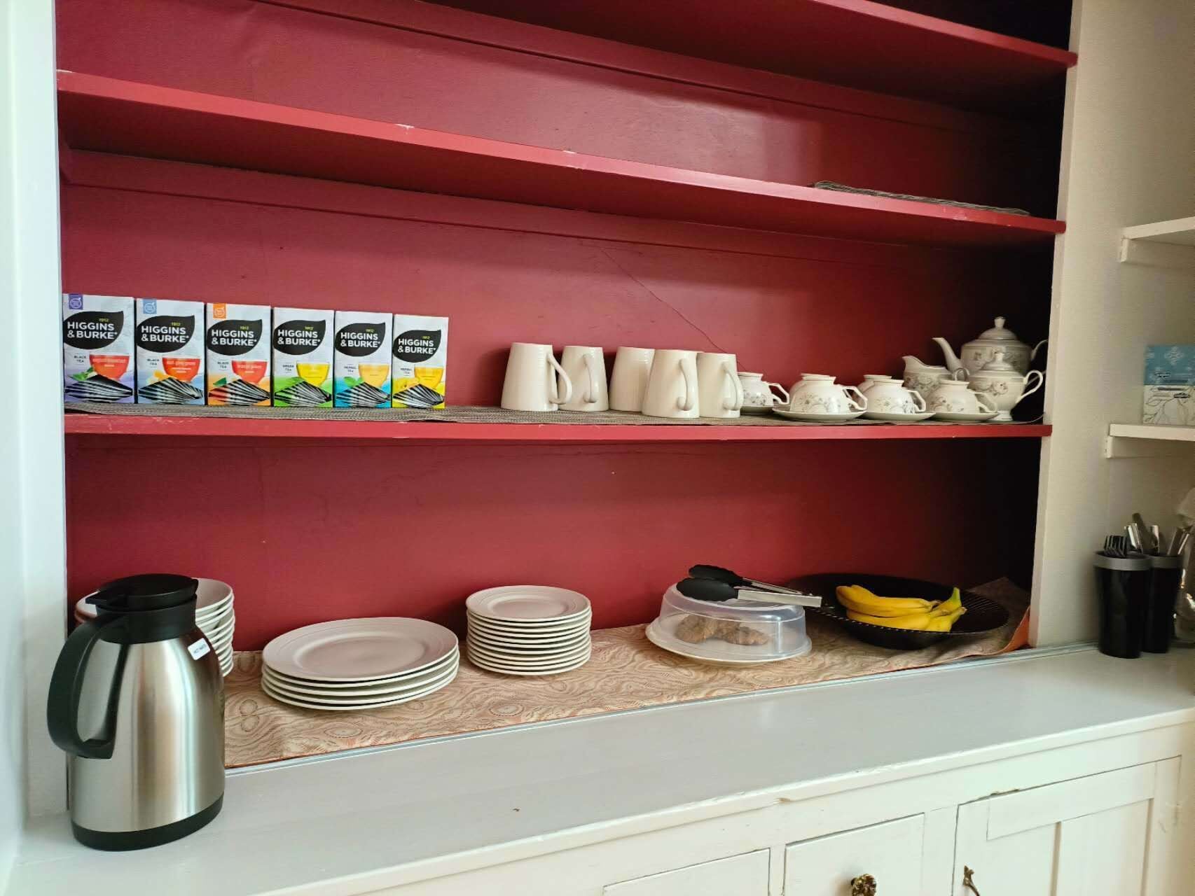 Una cocina con estantes rojos, armarios blancos y diverso menaje, incluyendo tazas, platos y una tetera.