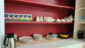 Una cocina con estantes rojos, armarios blancos y diverso menaje, incluyendo tazas, platos y una tetera.