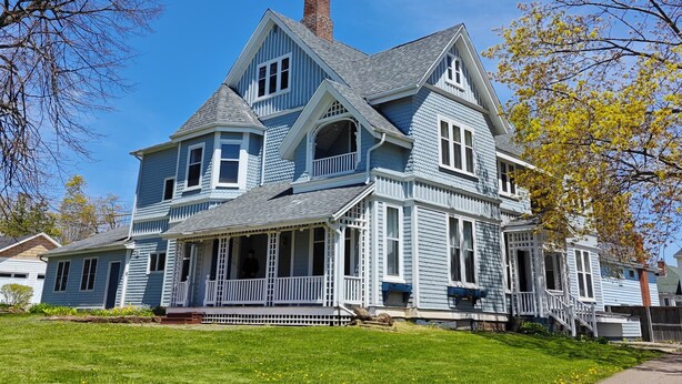 A large, two-story house with a wrap-around porch and a chimney. - Andy's Blue House (Charlottetown)