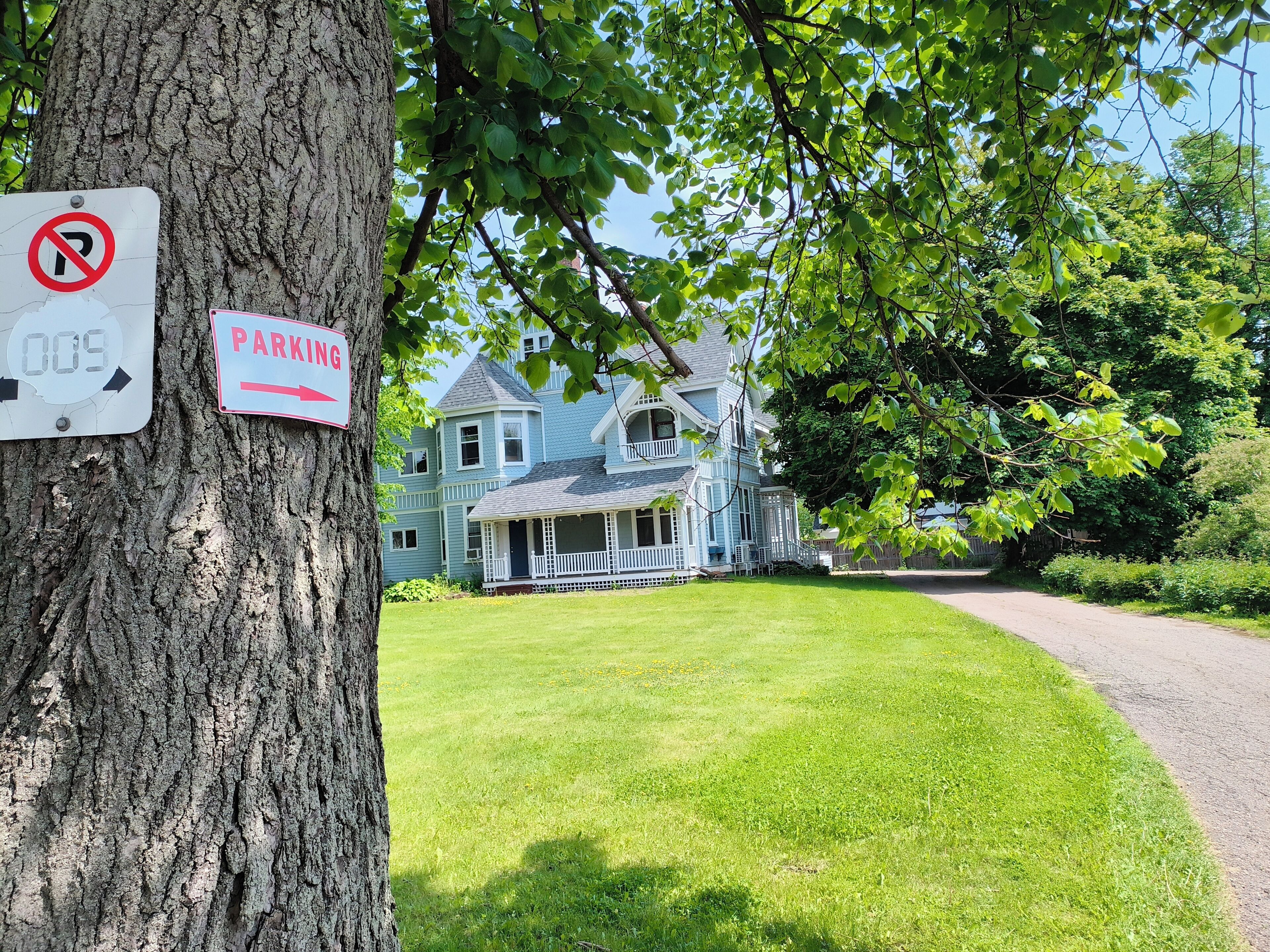 A large blue house with a porch, a no parking sign, and a parking sign.