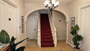 A grand staircase with a red carpet, flanked by white walls and framed pictures, leading to a door marked "Staff Only". - Andy's Blue House (Charlottetown)