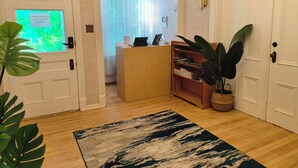 A hotel lobby with an exit sign, a reception desk, a wooden bookshelf, a potted plant, and a patterned rug. - Andy's Blue House (Charlottetown)