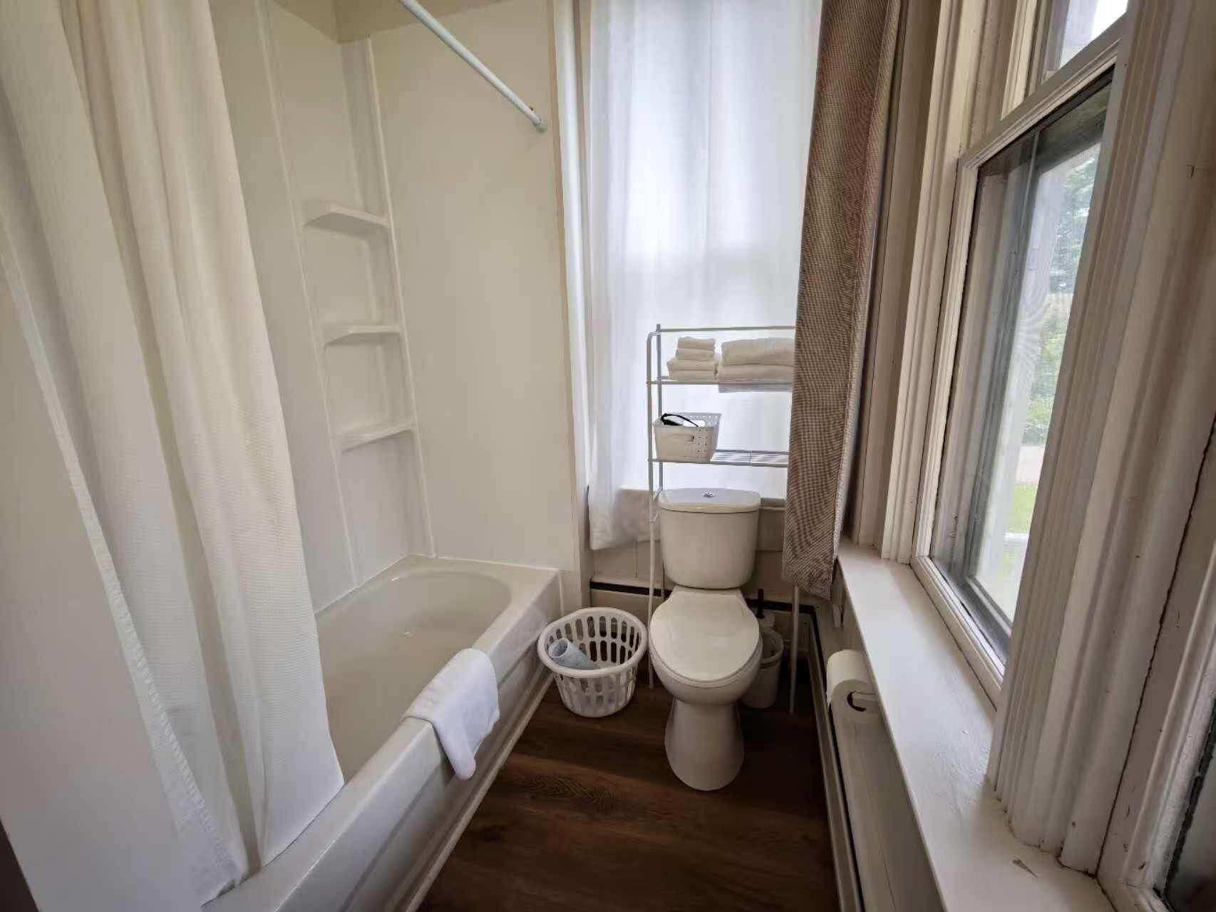 A compact bathroom with a shower, toilet, and a window.