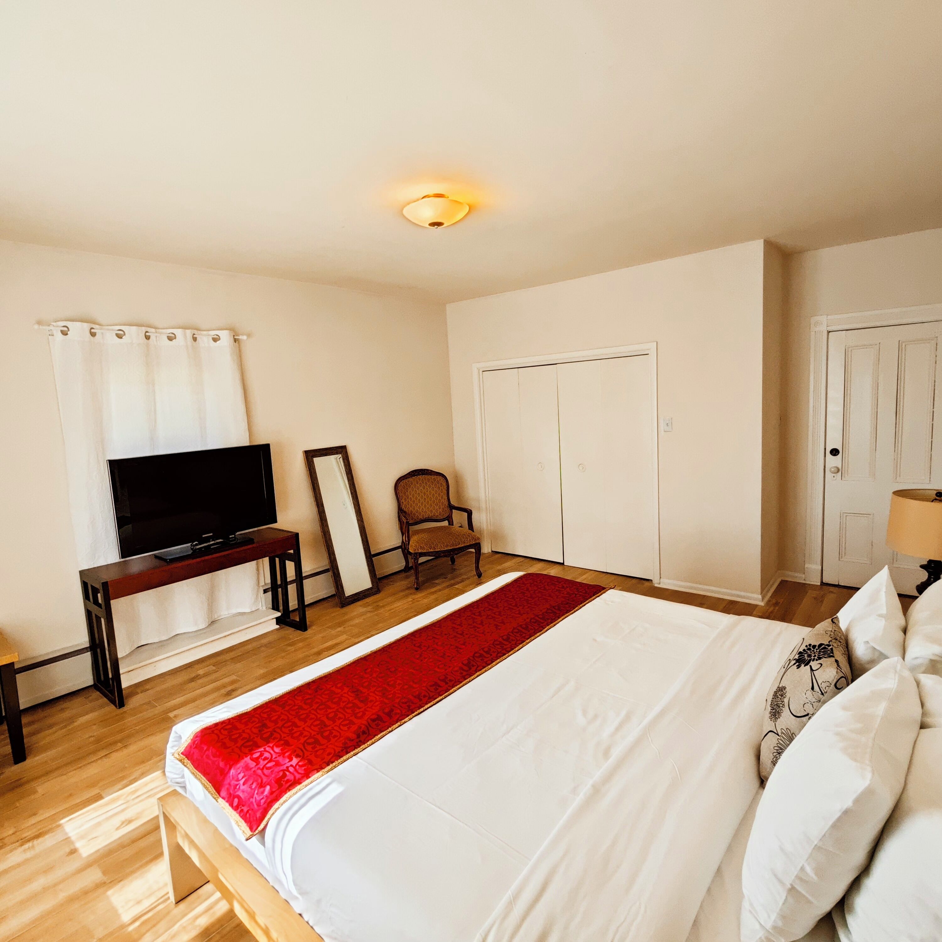 Une chambre à coucher avec un lit, une télévision, une chaise, une armoire et un tapis rouge.