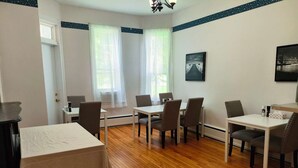 A modern, well-lit room with a dining area, a small kitchen, and a large window providing natural light. - Andy's Blue House (Charlottetown)