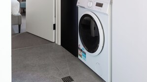 A laundry room with a front-loading washing machine and a top-loading dryer. - MAC Middle Park by Melbourne Apartment Collection (Middle Park)