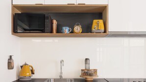 A modern kitchen with black cabinets, a stainless steel sink, and a built-in oven. - MAC Middle Park by Melbourne Apartment Collection (Middle Park)