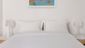 A neatly made bed with white linens, two bedside lamps, and a framed tropical-themed painting on the wall. - MAC Middle Park by Melbourne Apartment Collection (Middle Park)