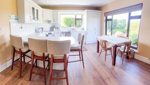 Una cucina moderna con mobili bianchi, un'area pranzo con sedie di legno e ampie finestre che danno su una vista verde.