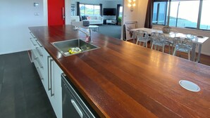 A modern kitchen with a wooden countertop, a built-in dishwasher, and a red door. - The King's Keep (Cable Bay)