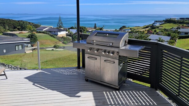 A barbecue grill on a wooden deck with a view of a coastal landscape. - The King's Keep (Cable Bay)