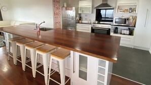 A modern kitchen with a central island, bar stools, a microwave, and a stove. - The King's Keep (Cable Bay)
