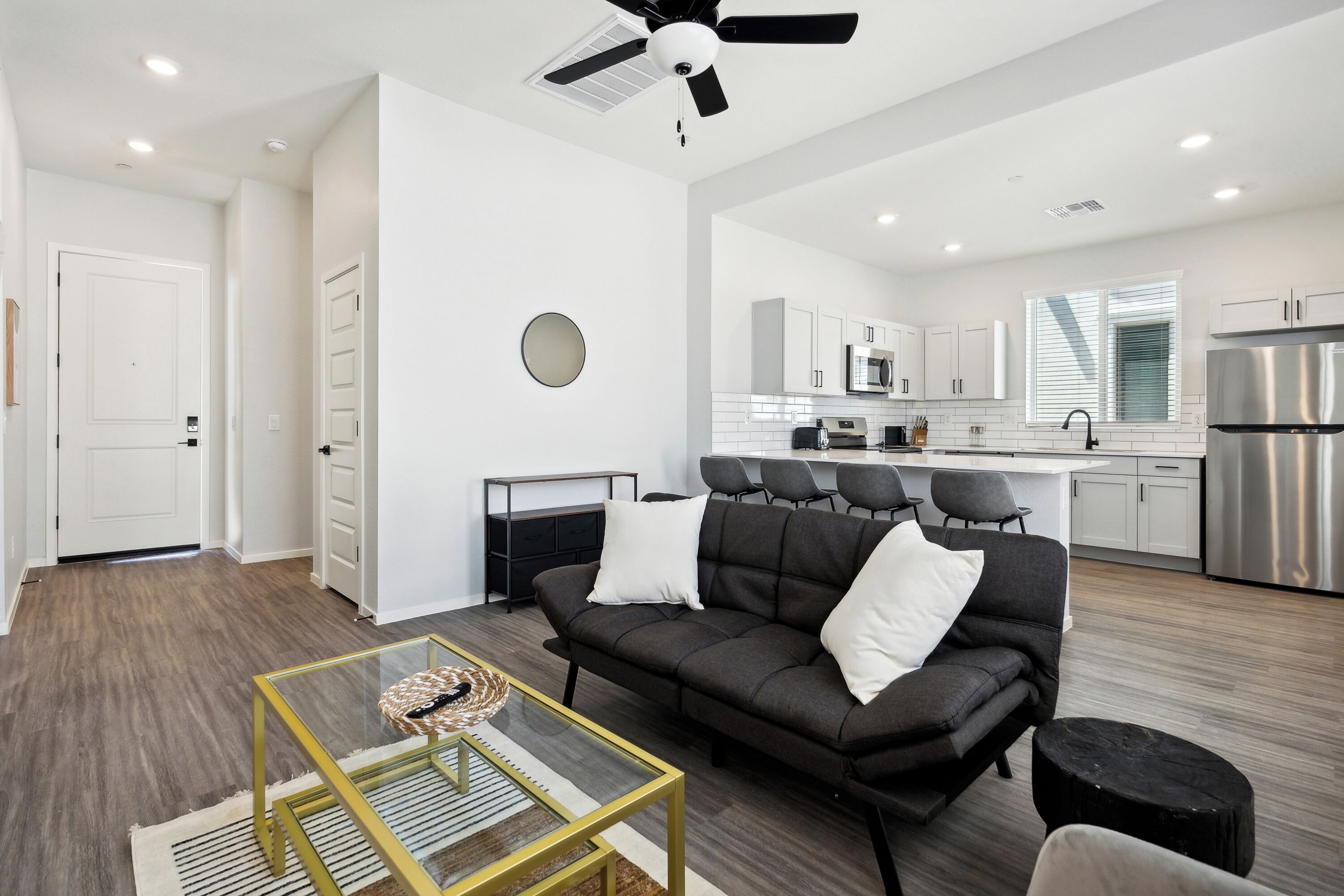 A modern living room with a sofa, a glass coffee table, and a ceiling fan.
