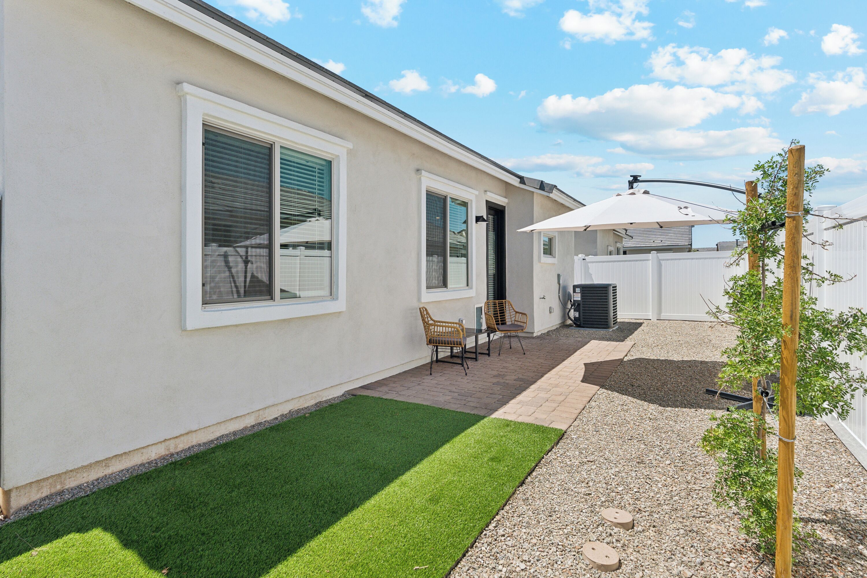 Un jardin à l’arrière d’une maison, avec une terrasse, une petite pelouse et une clôture blanche.