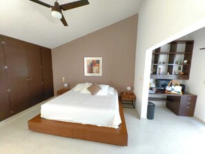 Ein Schlafzimmer mit einem großen Bett, einem Deckenventilator, einem Bild an der Wand und einem Schreibtisch mit Computer und Stauraum.