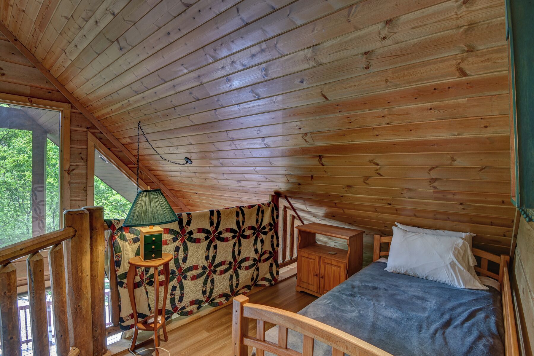 Una habitación de cabaña acogedora con techo de madera, una cama con manta azul, un tapiz acolchado y una mesita con lámpara.