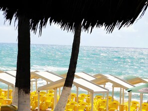 Ein Strand mit gelben Stühlen und einem strohgedeckten Gebäude.