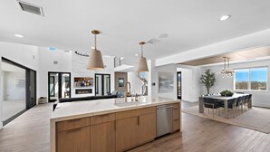 Een moderne keuken met een centraal eiland, hanglampen en een eetgedeelte met uitzicht.