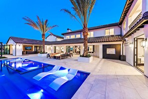 Een modern huis met een zwembad, terras en palmbomen.