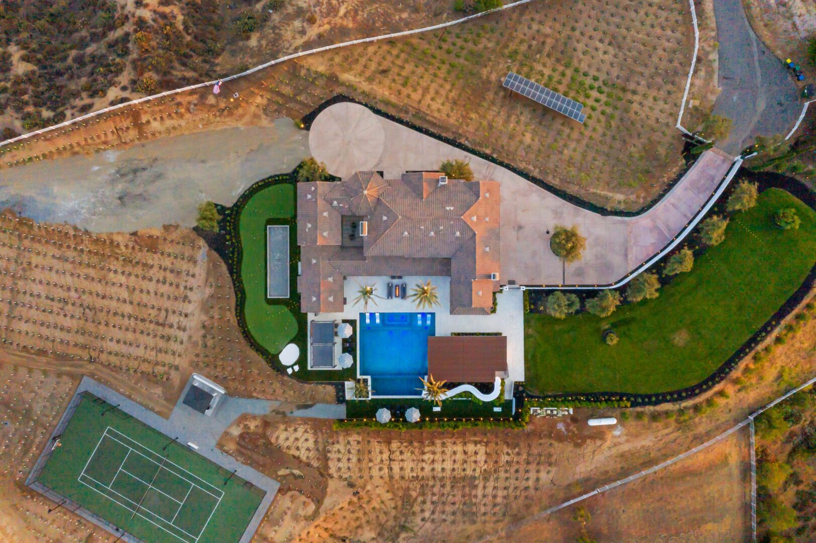 Vista aérea de una propiedad con piscina, cancha de tenis y jardines ajardinados.