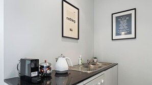 A modern kitchen with a black countertop, a kettle, a coffee maker, and a sink. There are two framed pictures on the wall.