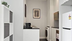 A modern kitchen with white cabinetry, a built-in washing machine, and a coffee machine.
