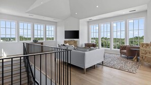 A spacious living room with a large sofa, a television mounted on the wall, and a staircase leading to an upper level. - Oceanview Oasis: Luxury 6BR Home with Pool (Seagrove Beach)