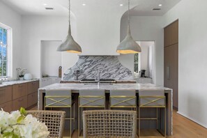 Een moderne keuken met marmeren aanrechtbladen, hanglampen en een centraal eiland met krukken.