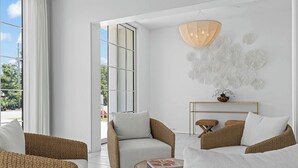 A modern living room with wicker furniture, a white sofa, and a round coffee table. - Oceanview Oasis: Luxury 6BR Home with Pool (Seagrove Beach)