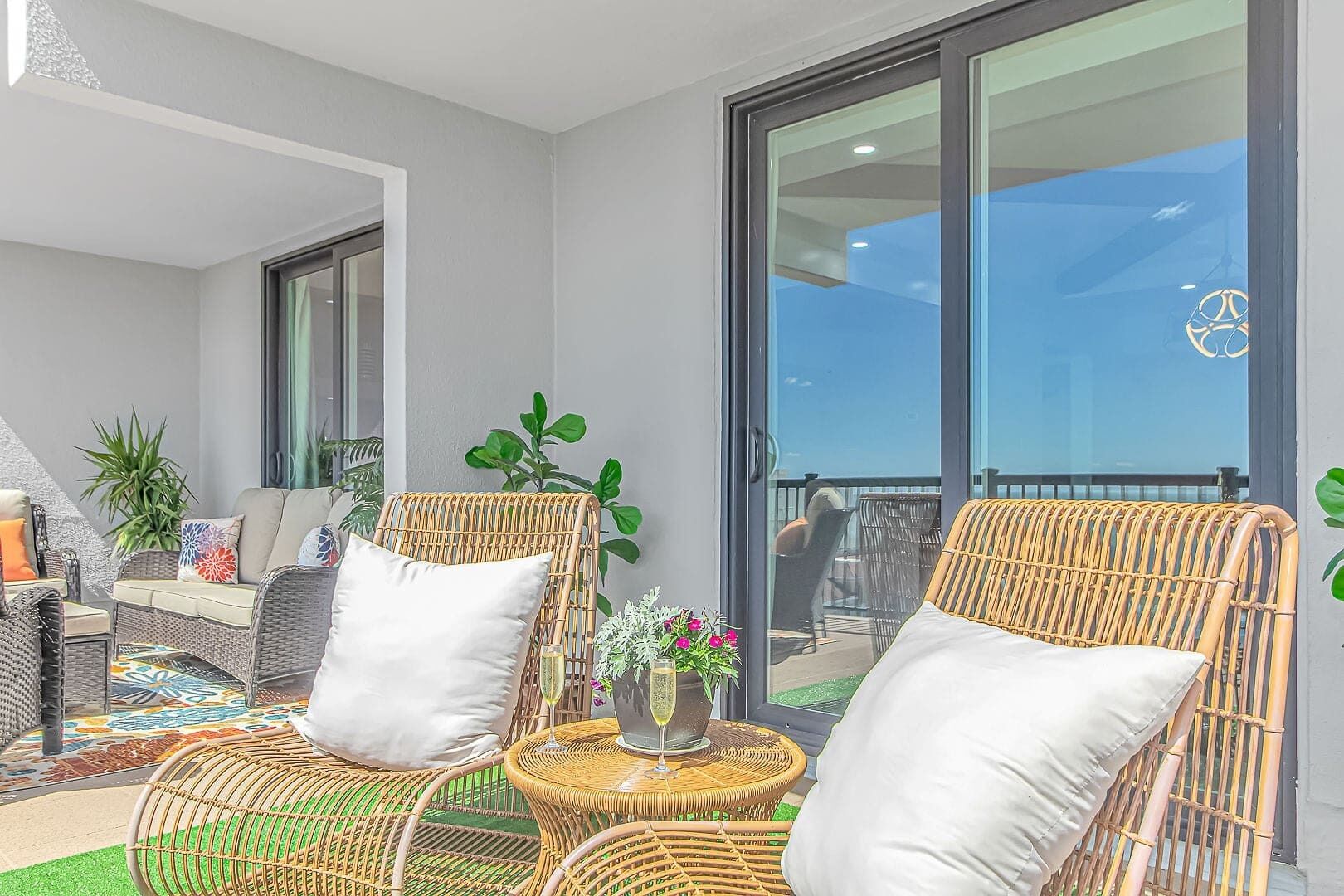 A balcony with wicker furniture, a glass door, and potted plants.