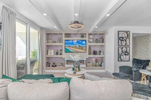 A living room with a sofa, a coffee table, a TV, and shelves with decorative items.