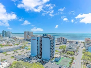 A high-rise hotel with multiple floors, a parking lot, and a view of the beach and ocean.