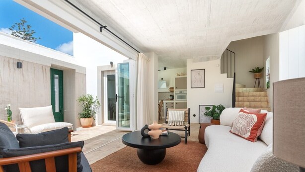 Una sala moderna con sofá, sillón y mesa de centro, un comedor con sillas y una escalera.