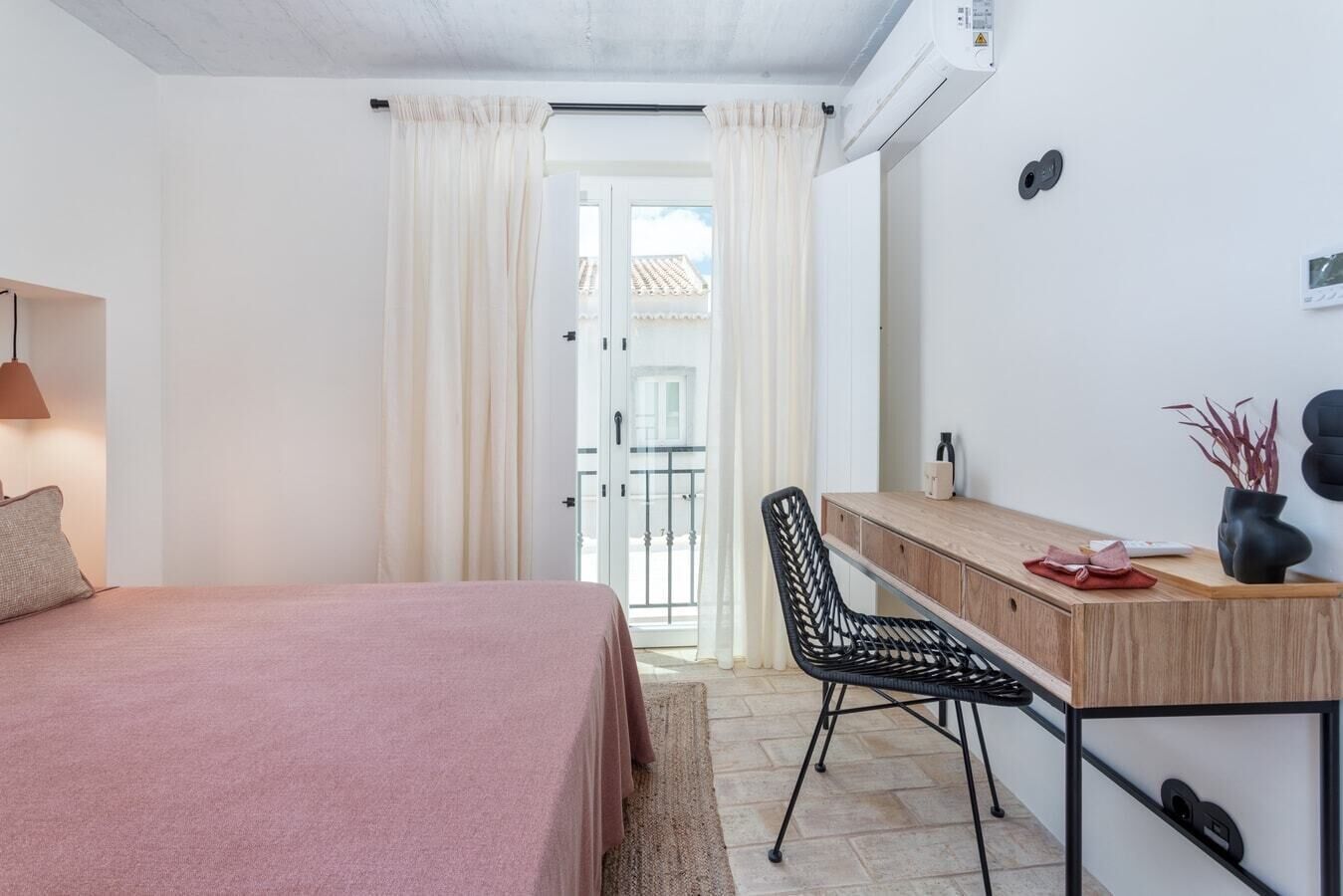 Ein Schlafzimmer mit Bett, Schreibtisch, Stuhl und Blick ins Freie.