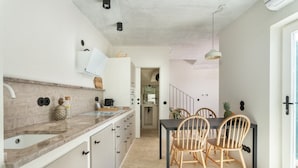 Cocina moderna con zona de comedor, que incluye una isla de cocina, sillas de madera y una escalera que sube a otro nivel.
