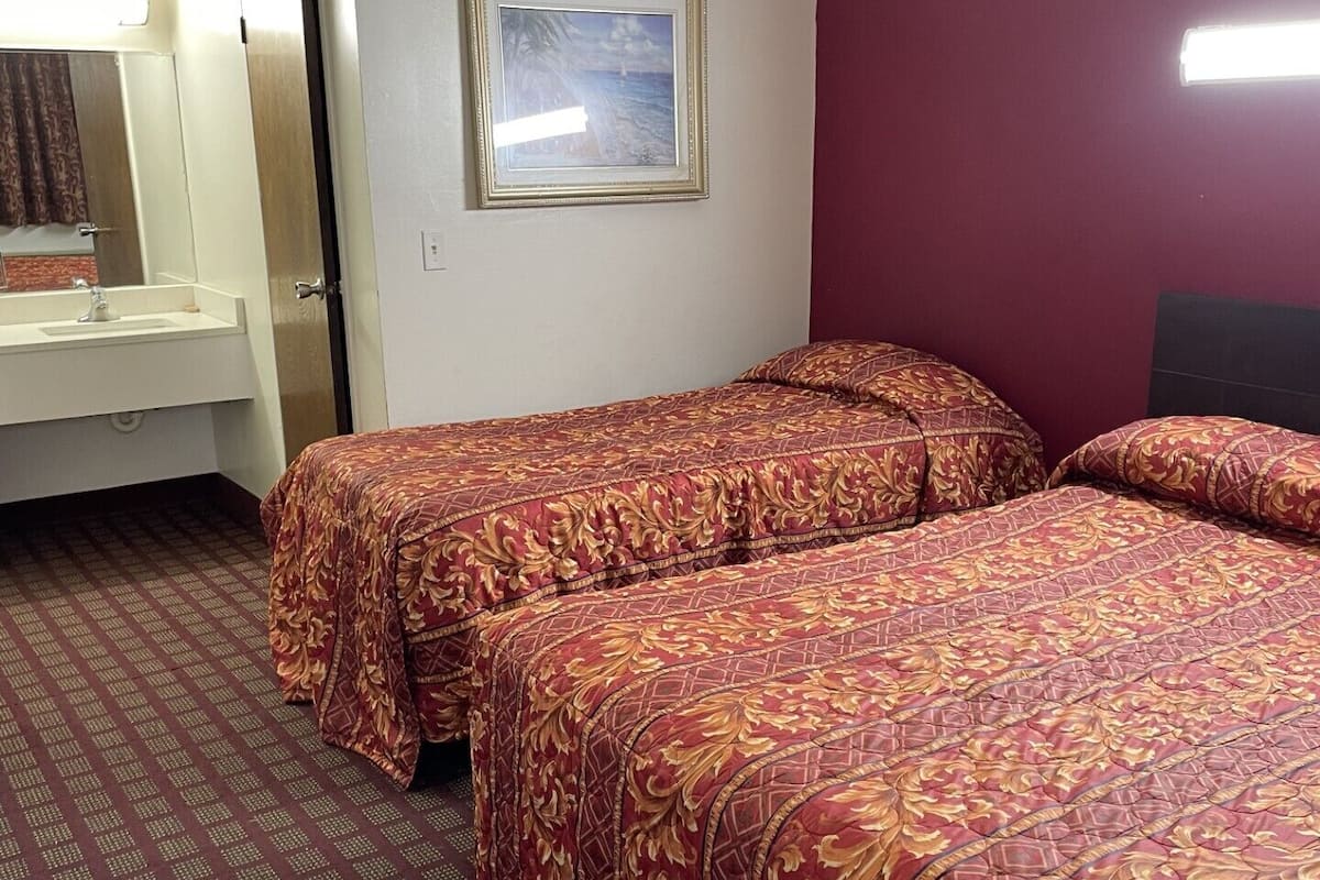 Ett hotellrum med två sängar, ett badrum och en inramad tavla på väggen.